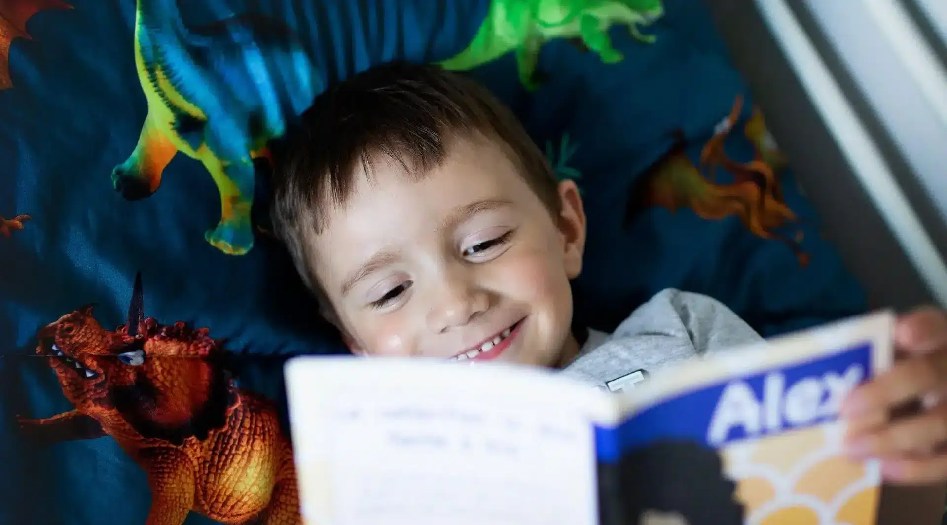 Un garçon lit un livre Facile à lire dans son lit en souriant.
